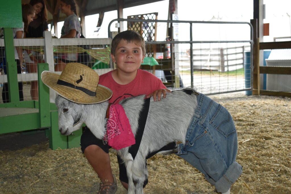 A young boy poses with his goat, which is dressed in a cowboy costume.